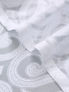 Macro view of white lace curtain fabric with intricate geometric floral textures and mesh