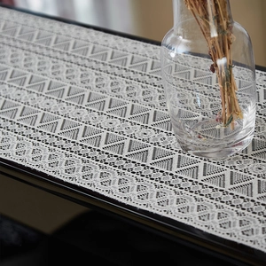 Detailed close-up of white lace table runner with geometric woven patterns and fringe