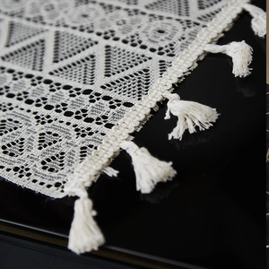Beige lace piano cover cloth with geometric patterns and handmade tassels on black background