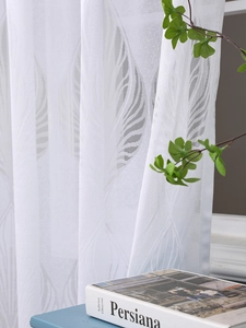 Detailansicht weißer Gardine mit Blätter-Jacquardmuster und feiner Netzstruktur am Fenster