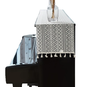Bohemian style beige lace table runner with tassels displayed on a black piano surface