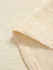 Macro view of beige jacquard curtain fabric showing geometric patterns and neat hem edges