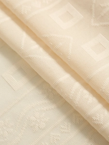 Close-up of cream white jacquard curtain fabric with geometric diamond texture and soft folds