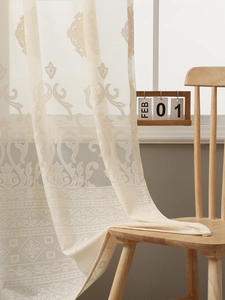 Detail of cream lace curtain with damask floral pattern and scalloped edge on wooden chair