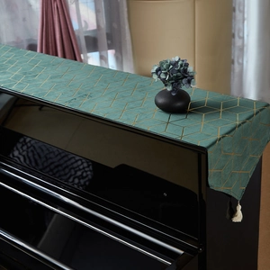 Close-up of emerald green piano runner with golden geometric patterns and white tassels