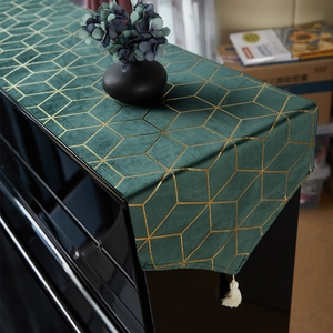 Dark green velvet piano cover with gold geometric pattern and white tassel accents