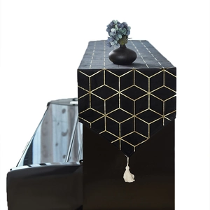 Black and gold linen piano cover with geometric patterns and elegant white tassels
