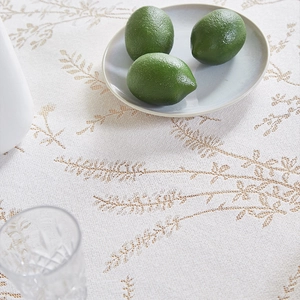 Close-up of white lace tablecloth with brown leaf patterns, lemon and glass on table