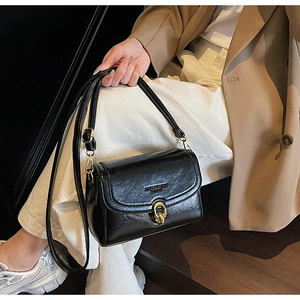 Détail d'un sac à bandoulière en cuir noir brillant avec boucle dorée sur un mannequin