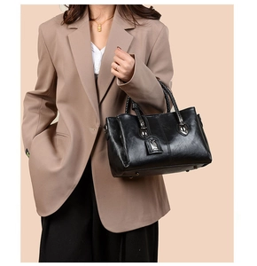 Detail of black faux leather tote with braided handles and metallic accents on business suit