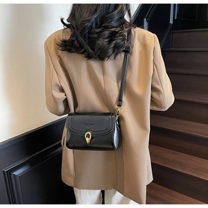 Détail d'un sac bandoulière en cuir noir brillant avec boucle dorée sur un modèle