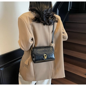 Détail du petit sac noir verni avec boucle dorée porté dans un escalier rétro