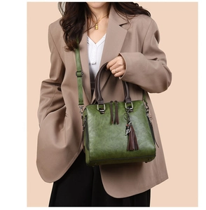 Detail of forest green leather tote bag with brown handles and silver feather pendant