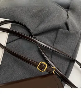 Détail de la bandoulière réglable en cuir marron foncé avec boucle dorée