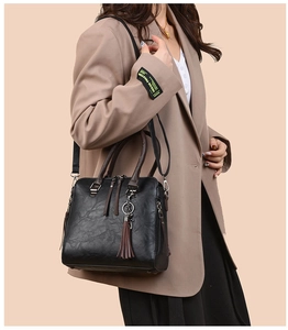 Detail of black pebbled leather tote bag with brown tassel and adjustable strap on model