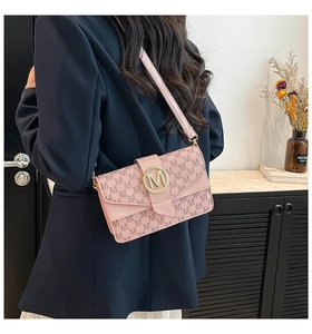 Detailed view of pink shoulder bag with M-pattern logo and gold metal hardware clasp