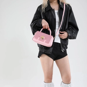 Pink crossbody handbag with glitter flap and metallic circular clasp on white background