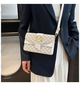 Close-up of white crossbody bag featuring grey M pattern and golden metal magnetic buckle