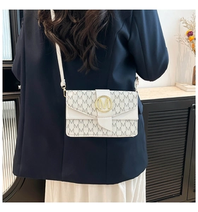 Detail view of white crossbody bag with M-pattern print and gold metal buckle on model