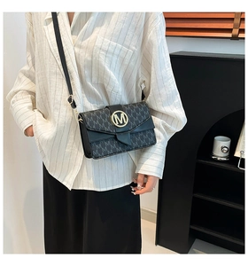 Close-up of golden M-shaped metal buckle and letter print on black crossbody bag