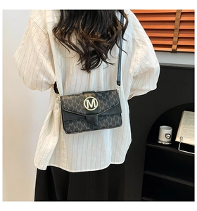 Detail view of the golden M-buckle on a black monogrammed leather crossbody bag