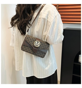 Close-up of brown crossbody bag with letter M pattern and golden metal buckle details