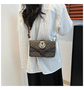 Detailed view of brown monogram crossbody bag with golden M buckle and leather trim