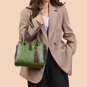 Retro green leather tote bag with brown handles and cat tassel charm worn by a model