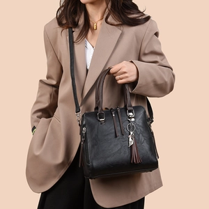 Chic black tote bag with brown handles and cat pendant, styled with a khaki blazer