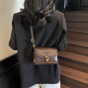 Sac à bandoulière rétro en cuir marron foncé avec boucle dorée sur un modèle minimaliste