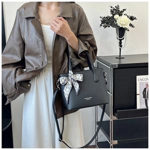 Détail d'un sac seau en cuir litchi noir avec texte doré et foulard en soie décoratif