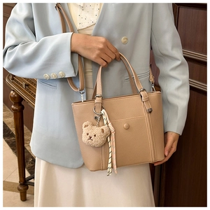 Détail d'un sac à main beige en cuir avec porte-clé ours en peluche et ruban à rayures