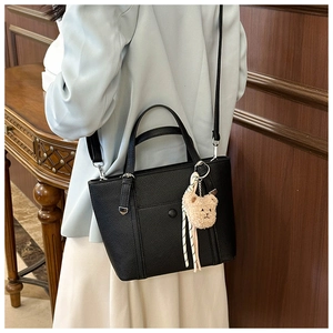 Sac seau noir à motif litchi avec pendentif ours porté par un mannequin
