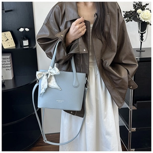 Détail du sac seau bleu clair en cuir texturé litchi avec un foulard en soie à motif cœur
