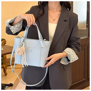 Vue détaillée du sac seau bleu clair avec breloque ours en peluche sur blazer gris