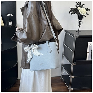 Détail d'un sac seau en cuir bleu clair avec foulard à cœurs et lettrage doré