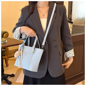 Détail du sac seau bleu clair en cuir grainé avec pompon décoratif et bandoulière amovible