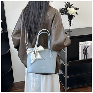 Détail du sac seau en cuir bleu clair avec motif litchi, foulard floral et boucles en métal