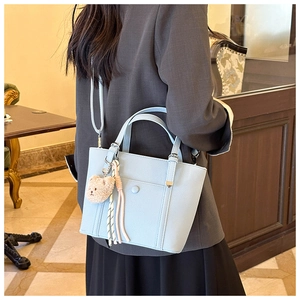 Détail du sac à main bleu clair avec cuir texturé, breloque d'ours en peluche et cordon tressé