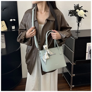 Détail du sac seau en cuir vert clair avec un foulard imprimé cœur noué sur la poignée