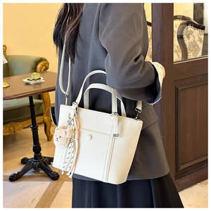 Détail d'un sac seau en cuir crème avec un charm ours en peluche et gland décoratif