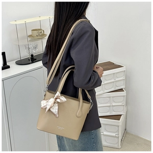 Détail d'un sac seau beige avec texture grainée et poignée en foulard de soie sur un modèle