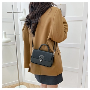 Detail of a black crossbody box bag with woven texture lid worn by a model in a brown suit
