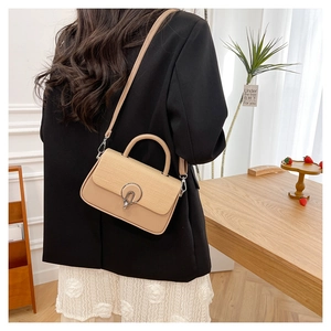 Detail of beige leather bag with woven texture flap and metallic circular buckle