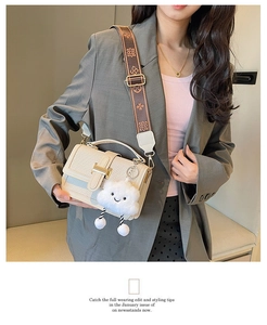 Off-white woven shoulder bag with wide geometric strap and plush charm on grey blazer
