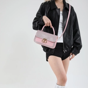 Pink sequin crossbody bag with gold metal clasp carried by model in leather jacket