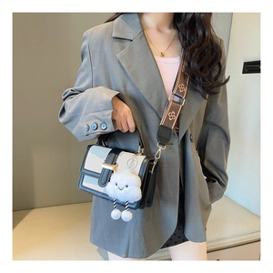 Detail of color-block square bag with gold buckle, wide patterned strap and plush charm