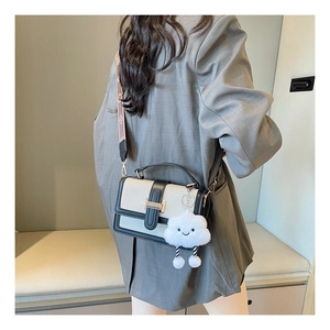Detail of cream woven handbag featuring black leather trim and decorative plush cloud charm