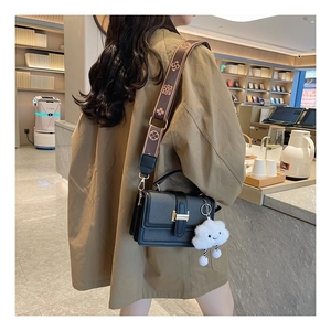 Detail of black leather crossbody bag with wide floral strap and plush cloud charm