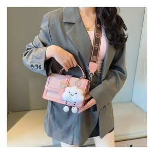 Detail of pink woven crossbody bag with gold buckle and plush cloud charm on grey suit